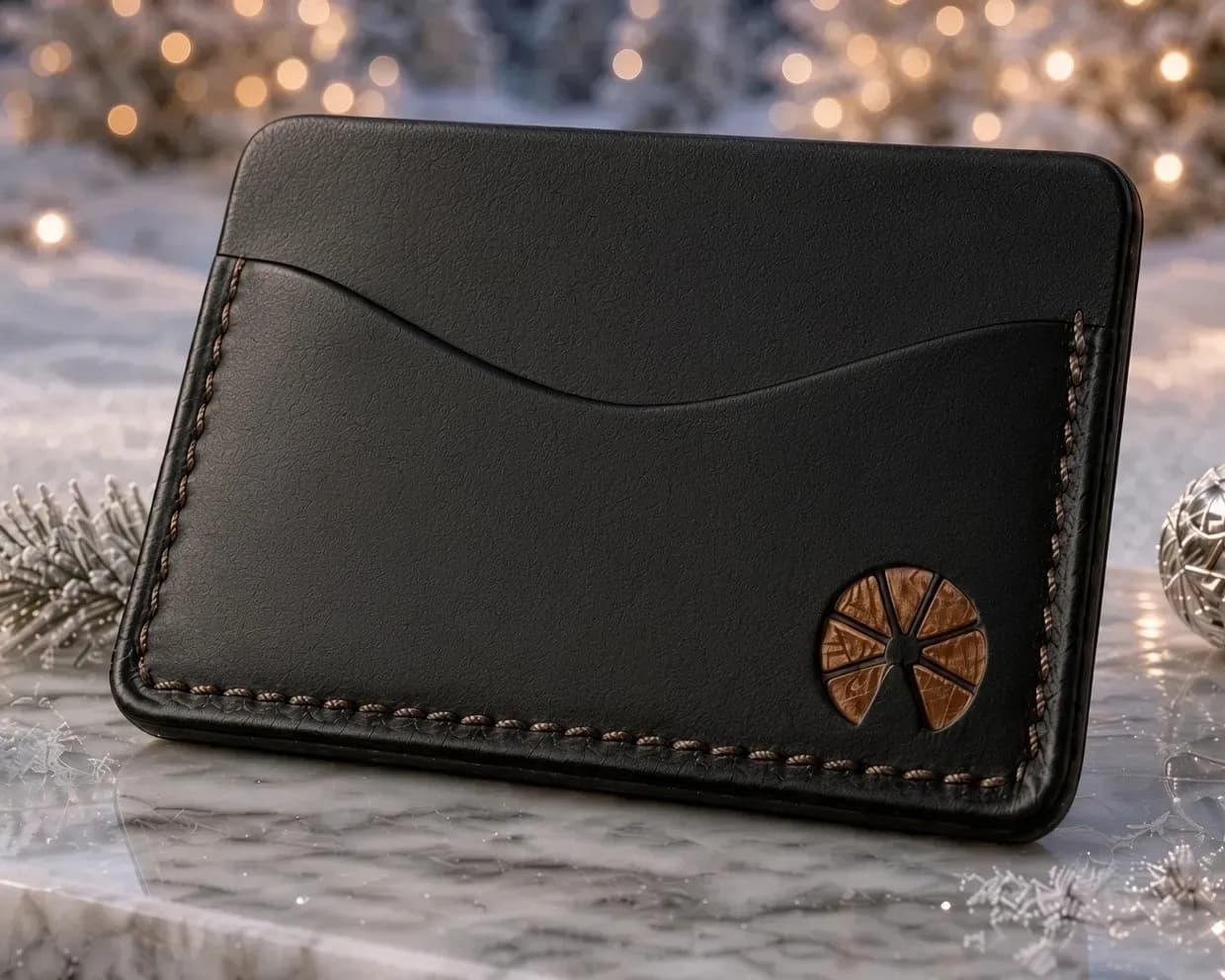 The Club Orange Cold Wallet, black leather with orange stitching, on marble in the snow