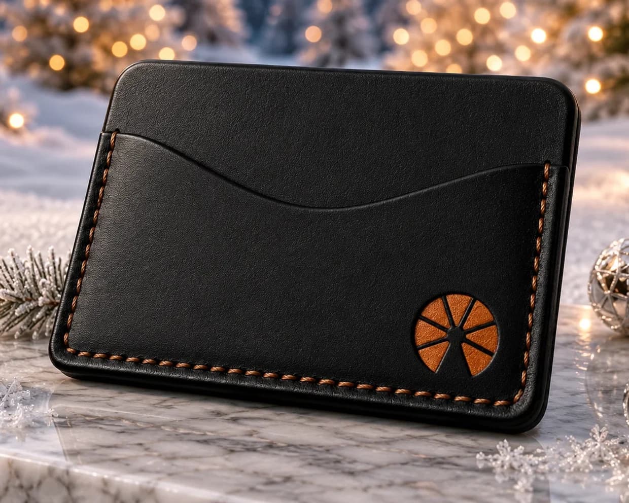 The Club Orange Cold Wallet, black leather with orange stitching, on marble in the snow
